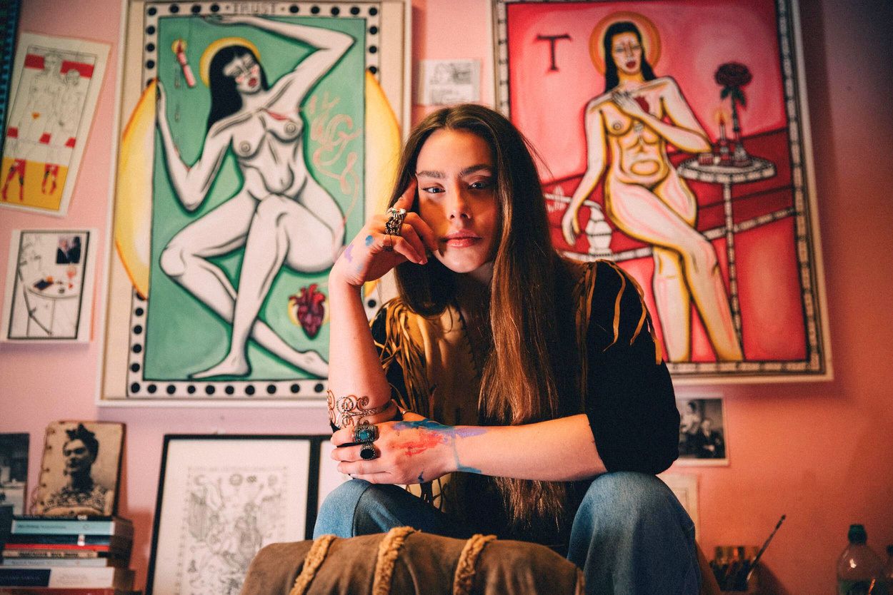 Kim Mac sitting in her studio in front of two of her paintings.
