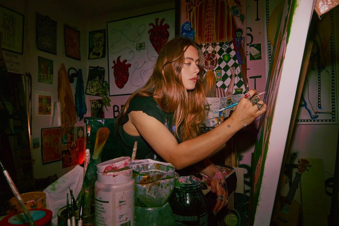 Kim Mac painting at an easel, surrounded by paint pots and her canvases.